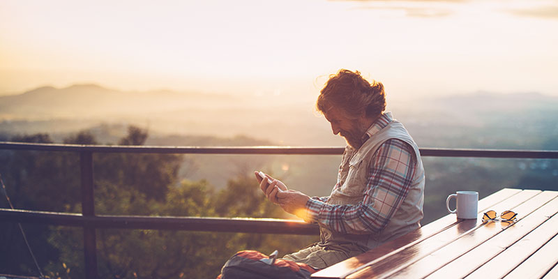 a man using his cellphone while sitting with a view of the mountains at sunset